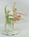 Grupo escultórico Art-Deco, em porcelana alemã, marca da manufatura Rudolstadt Volkstedt, policromado, representando "Dançarinas". Apresenta um dedo colado. Med. 27,5x25x9cm.