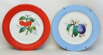 Par de pratos decorativos em porcelana, decorados com pinturas de frutas ao centro em policromia. Um com aba na cor azul e outro laranja. Diam. 20 cm.