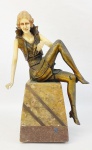 Escultura estilo art-deco representando "Dama sentada". Vestes e pernas em metal dourado. Rosto e braços em resina. Base em mármore rajado, de dois tons. Alt. total 21,5 cm.