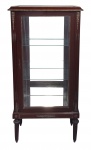 Vitrine estilo Luis XVI, em madeira. Tampo, laterais e porta com vidro. Interior com base e fundo com espelho e 2 prateleiras em vidro. Apliques e guarnições em bronze trabalhados com figuras e folhagens. Pernas torneadas e frisadas afinando para baixo. Med. 132,5x65x32 cm.