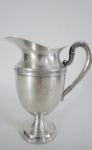 Elegante jarra em metal espessurado a prata, bojo balaústre liso. Med. 16 cm alt.