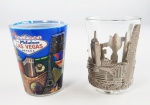 2 copos shot em vidro, sendo um com suporte em metal de alguns pontos turísticos de Hong Kong e de Las Vegas. Medidas aproximadas altura 6,5 cm e diâmetro 4,5 cm e altura 6 cm e diâmetro 5 cm