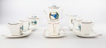 Jogo para café em porcelana na cor branca com simbologia representando o II Congresso Eucarístico Estadual, contendo 1 bule, 1 açucareiro, 1 cremeira e 6 xícaras com pires. Medidas aproximadas bule altura 17 cm e largura 16,5 cm, açucareiro altura 10,5 cm e largura 13 cm, cremeira altura 8 cm e largura 10,5 cm, pires 8,5 x 8,5 cm, xícara altura 5 cm e diâmetro 4,5 cm