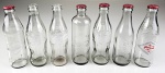 7 garrafas Coca-Cola em vidro (230 ml), 5 garrafas com tampa e 2 garrafas sem tampa. Medida aproximada altura 19,5 cm