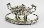 BELO CENTRO DE MESA/FLOREIRO EM PRATA DE LEI COM MARCAS PARA PORTUGAL, ÁGUIA, 1. TITULO TEOR 916. CAPRICHADOS ROCAILLES E CONCHEADOS RELEVADOS. ASSENTE SOBRE PRESENTOIR COM ESPELHO BIZOTADO. PORTUGAL, INICIO DO SEC. XX. 38 CM DE COMPRIMENTO. 2580 G