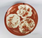 KUTANI  FORMIDÁVEL MEDALHÃO DE GRANDE DIMENSÃO DECORADO COM FUNDO NA TONALIDE ROUGE DE FEURS REMATADO EM OURO E RESERVAS COM FLORES E PÁSSAROS. DECORADO TAMBÉM NA PARTE INFERIOR. JAPÃO, INICIO DO SEC. XIX. 46 CM DE DIAMETRONOTA: Kutani-yaki é uma cerâmica com pintura sobre esmalte, feita nas cidades do sul de Kanazawa, Komatsu, Kaga e Nomi na província de Ishikawa. Com suas cores vivas, ele atraiu muitos fãs no exterior, e muitos dos tipos relativamente novos de Kutani-yaki são exportados, então alguns de vocês já devem estar familiarizados com ele. A história de Kutani-yaki remonta ao século XVII. O primeiro lorde do Domínio Daishoji, Maeda Toshiharu, disse a seu criado Goto Saijiro para aprender sobre a cerâmica em Hizen-arita, depois que a magnetita foi descoberta em Kaneyama, Kutani, que agora é Sannaka cho, Kutani na Prefeitura de Ishikawa. Ele adotou suas técnicas e construiu um forno em Kutani, que se diz ser o início do Kutani-yaki . Com o uso requintado de muitas cores vivas, como azul, verde e amarelo e padrões ousados e não convencionais, Kutani-yaki veio em muitas formas. Ela logo recebeu grande aclamação como a melhor representação de porcelana com pintura overglaze no Japão, ganhando elogios em particular por sua singularidade e a poderosa beleza de suas formas. No entanto, o forno em Kutani foi repentinamente fechado por volta de 1730. O motivo ainda é desconhecido até hoje, e a verdade ainda não foi descoberta, embora corram rumores de que isso tem algo a ver com "problemas nos negócios". Os mistérios que cercam Kutani-yaki podem ser mais um fator que torna as pessoas atraídas por ele. Os que foram feitos antes desse incidente são chamados de Ko (antigo) kutani para diferenciá-los daqueles feitos depois. Cerca de 80 anos após o fechamento do forno, o forno Kasugayama foi inaugurado em Kanazawa sob a gestão direta do Domínio Kaga. Na mesma época, uma nova pedra de porcelana foi descoberta na área próxima, o que impulsionou ainda mais o renascimento, e Kaga Domain, que costumava obter suas cerâmicas de outros países, protegeu a indústria local ao proibir a importação de porcelana e cerâmica. Durante a era Meiji, o Saishoku-kinrante de Kutani Shoza tornou-se popular e o Kutani-yaki tornou-se um produto de exportação importante. Apresentado em exposições como a Weltausstellung 1873 Wien, facilitou a comunicação internacional e, desde então, Kutani-yaki adotou métodos ocidentais em seu processo de produção, expandindo-se estrategicamente no mercado global.
