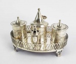FORMIDÁVEL TINTEIRO ESCRIVANINHA EM  PRATA DE LEI SETECENTISTA. BATIDO E CINZELADO. BASE COM GRADIL FENESTRADO. ELEVADO SOBRE QUATRO PÉS. DOTADO DE DOIS TINTEIROS DE GRANDE PORTE COM SUAS TAMPAS, UM GRANDE ARIEIRO COM TAMPA, UM CANUDO PARA PENAS E UM CASTIÇAL. ESSES GRANDES TINTEIROS COM CAPACIDADE PARA ATENDER ALTA DEMANDA ERAM EMPREGADOS EM REPARTIÇÕES PÚBLICAS E MESAS DIRETORAS DE ORDENS RELIGIOSAS. ALÉM DE ATENDEREM AO GRANDE VOLUME DE TRABALHO CO PARA CONCORRIAM PARA O RITUAL DA POMPA DAS LAVRATURAS A QUE SE DESTINAVAM. A ELEGANTE EXECUÇÃO EM FORMAS E NOS ARREMATES DOS CAPRICHADOS CINZELADOS ESTILO DOM JOSÉ I COM GUIRLANDAS FLORAIS E FAIXAS DENOTA TER  SIDO ENCOMENDADO PARA USO EM LOCAL DE GRANTE APARATO. EXEMPLAR SEMELHANTE A ESSE UTILIZADO AINDA NO GOVERNO DE DOM JOÃO VI NO MINISTÉRIO DA GUERRA E ESTÁ EXPOSTO NAS COLEÇÕES DO MUSEU HISTÓRICO NACIONAL , TAMBÉM REPRODUZIDO NA PAGINA 202 DO LIVRO O OFICIO DA PRATA NO BRASIL DE  HUMBERTO FRANCESCHI. BRASIL, SEC. XVIII. 24 CM DE COMPRIMENTO. 1235 G