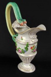 HEREND PRINTEMPS   BELO E RARO JARRO PARA ÁGUA PADRÃO PRINTEMPS. LINDA ALÇA LATERAL DUPLA COM FEITIO DE VISTOSAS SERPENTES. DECORAÇÃO COM GUIRLANDA FLORAL RELEVADA E FLORES PINTADAS EM ESMALTE. ARREMATES EM OURO. TERÇO INFERIOR COM GOMADOS RELEVADOS. MARCAS DA MANUFATURA SOB A BASE. PEÇA PARA COLECIONADOR! HUNGRIA, INICIO DO SEC. XX. 30 CM DE ALTURA.NOTA: A Herend Porcelain Manufactory é uma empresa de fabricação húngara, especializada em porcelana de luxo pintada a mão e dourada. Fundada em 1826, baseia-se na cidade de Herend perto da cidade de Veszprém. Em meados do século 19, foi fornecedora da dinastia Habsburg e aristocráticos clientes em toda a Europa e muitos de seus padrões clássicos ainda estão em produção. O apelo artística e o esforço de fabrico das primeiras peças conseguiu em curto espaço de tempo notabilizar a manufatura. Assim foi premiada em importantes exposições como A primeira Exposição Húngara de Arte Aplicada , a Exposição de Viena , em 1845, a Grande Exposição de Londres de 1851, a Exposição da Indústria de Todas as Nações , em Nova York, 1853 e a Exposição Universal de Paris de 1855. Esses prêmios trouxeram valorização para Herend. Esta apreciação aparece nas encomendas feitas em nome de vários cortes reais ( Rainha Victoria , Francisco José I. , Maximiliam ( imperador mexicano) dentre outros). O nome dos padrões conhecidos referem-se aos primeiros clientes ( Rainha Victoria , Esterházy, Batthyány , Rothschild ,Apponyi ). Em 1865 Francisco José I deu título para de nobreza para Mór Fischer, apreciando seus resultados e trabalho em arte de porcelana. A partir de 1872 Mór Fischer Farkasházy , produzindo para a Corte Real, tinha o direito de usar as formas e padrões da Manufatura de Viena, que tinha fechado. Essa foi a idade de ouro de Herend. Os artistas de projeto, oleiros, pintores e modeladores adicionaram valor a marca que recebeu 24 grandes prêmios de ouro em exposições mundiais entre 1851 e 1937. Talvez o padrão Herend mais conhecido foi apresentada na Exposição Mundial de Londres, em 1851, com ramos floridos pintados em alegres, cores vivas. A rainha britânica, Victoria , ordenou um jantar com o serviço desse padrão ganhador da medalha de ouro no Castelo de Windsor. Daí o nome do padrão ser "Viktória".
