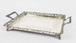 BELO TABULEIRO EM PRATA DE LEI TEOR 833. FEITIO RETANGULAR, COM GALERIA FENESTRADA. ALÇAS LATERAIS REMATADAS POR FLORES. PLANO COM GUILLOCHES. ASSENTE SOBRE QUATRO PÉS EM GARRA. BRASIL, SEC. XX. 22 CM DE COMPRIMENTO. 660 G