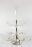 WMF  PORTENTOSO EPERGNE EM METAL EPESSURADO A PRATA. CONSTRUIDO EM TRES ESTAGIOS O ULTIMO COMO FLOREIRO. O CRISTAL É COM BELA LAPIDAÇÃO . SÃO QUATRO PRATOS NA BASE, UM MAIOR INTERMEDIÁRIO E A ÚLTIMA COM FEITIO DE CORNETA PARA  CONTER FLORES. MARCAS DA MANUFATURA. ESTÁ IMPECÁVEL. ALEMANHA, INICIO DO SEC. XX. 64 CM DE ALTURANOTA: A palavra epergne é tirada do francês epargne, que significa economia, e originalmente exibiu a aparência de ortografia mais anglicizada. A epergne inglesa economiza de duas maneiras. Primeiro, na economia de espaço precioso: o costume de serviço no sec. XVIII e inicio do XIX requeria que grande parte dos alimentos fossem colocados na mesa ao mesmo tempo. Os comensais que entram na sala de jantar encontraram a comida no lugar, geralmente em pratos de entrada cobertos (os pratos, às vezes, eram colocados sobre um recheou térmico com água quente), e era composto por um ou dois tipos de peixe e uma ou duas sopas. Além disso, por volta de 1760, tornou-se moda para o anfitrião esculpir o pássaro ou outro animal que fosse a opção de carne na mesa (lembra-se dos filmes em que as mesas tinham porcos inteiros, pássaros com penas para enfeitar montados no centro?).A segunda maneira em que economiza a epergne é que ela torna econômico o uso de nozes raras, frutas, condimentos e outros luxos dos trópicos. Os convidados se serviam da epergne, e as iguarias que não eram comidas ficavam intocadas nas mesas centrais, em vez de serem desperdiçadas quando os pratos fossem limpos no serviço convencional. Assim as EPERGNES podem conter frutos, doces, petiscos e outras iguarias para serem consumidas com os dedos e também se prestam para decoração com flores. A partir do período vitoriano a epergne foi aliviada de sua grande posição de servidor.No "novo" estilo de serviço, a la russe, cada prato era trazido separadamente em sequencia, deixando mais espaço para a exibição de flores neste acessório. O final do século XIX e início do século XX viu um breve e limitado ressurgimento de epergnes nos estilos rococó e neoclássico, ainda assim, estes foram destinados a serem usados como objetos decorativos, não propriamente para servir.