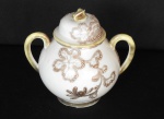 Açucareiro, finíssima porcelana japonesa creme. Policromia: personagens típicos. 13x10cm. Conservado; imperceptível lasca em uma das pétalas que ornamentam a pega do tampo. Peônias e ramas em relevo, realces dourados.