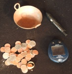 Lote com peças diversas, entre elas uma pequena panela decorativa de cobre, uma caneta e medidor de glicemia no estado, e moedas diversas..