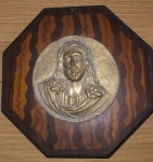 Quadro octogonal em madeira nobre com medalhão alusivo à face de Cristo em bronze. Medalhão rico em detalhes aplicado mede 12,5 cm de diâmetro e placa de madeira 23x23cm.
