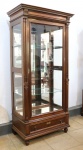 MOBILIÁRIO - Vitrine estilo império, em madeira nobre (vinhático) com porta e laterais em vidro, prateleiras internas e fundo espelhado. Gaveta inferior com entrada de chaves em bronze. Med. 223x107x64 cm.