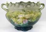 FAIANÇA ALEMÃ - Cachepot genuinamente art nouveau em faiança alemã do séc. XIX., nas cores verde degrade sobre fundo branco ao entro esmaltado com flores do campo, alças laterais com delicados movimentos, borda recortada acompanhando a silueta das flores em relevo, friso dourado. Med. 32x48x35 cm. Apresenta fios de cabelos.