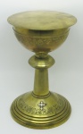 Cálice litúrgico com patena em metal banhado de dourado, com trabalhos de parreiras e cachos de uva, tendo na base cruz em relevo. Alt. sem a patena 20,5 cm.