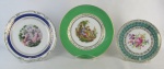 Três pratos decorativos em porcelana, sendo um da manufatura Schmidt decorado com ninfas ao centro, um Mauá com cena galante e um alemão da manufatura Bavaria, com flores e folhas em policromia. Detalhes em dourado. Diam. maior e menor 24,5 e 19,5cm.