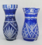 Dois vasos em cristal nas tonalidades azul e translúcida. Lapidações dedão e sulcos bisotados. Um apresenta pequenos bicados na base e trincado na borda. Alts. 17 e 15,5 cm.