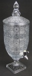 Grande refresqueira em demi cristal translúcido, lapidado com rosetas e sulcos em relevo. Base de seção quadrada. Torneira em material sintético. Alt. 51cm.