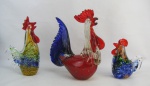 Três estatuetas em murano policromado, representando "Três galos". Apresentando um pó de cobre internamente. Dois apresentam pequeno bicado. Alts. 26 e 15,5cm.