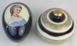 Duas caixas em porcelana, sendo uma oval no tom azul cobalto, com busto feminino em policromia sobre a tampa, e a outra circular italiana com marca da manufatura Keramos na base, decorada com flores e folhagens em policromia. Caixa oval com pequena colagem na borda. Meds. 12x18,5x12,5 e 13x16cm.