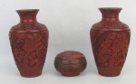 Três peças em laca no tom vermelho, com trabalhos de flores, folhas e arabescos em relevo, sendo par de vasos e pequena caixa. Um vaso com minúsculos restauros. Alt. vasos 12,5cm.