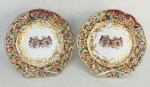 Par de pratos brasonados, de coleção, em porcelana italiana, com marca da manufatura de Napoles e as inscrições "Asa Mageste', Lé empereur d' Autriche", no verso. Abas decoradas com cenas de figuras em relevo, e ao centro brasão. Detalhes em dourado. Um apresenta restauros. Diamts. 20cm.