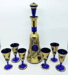 Elegante conjunto de licoreiro e 6 taças em vidro veneziano, na cor azul cobalto, ricamente decorados com pinturas a ouro. Alts. 29,5cm (licoreiro) e 9,5cm (taças).