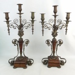 Raro e antigo par de candelabros, estilo medieval, para três velas, em madeira e metal patinado, com trabalhos de folhas, elos, volutas e gomos. Alt. 57cm.