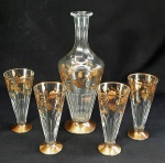 Conjunto em cristal lapidado e detalhes em ouro brunido composto por garrafa e 4 copos altos tipo tulipa. Med. 32 e 16 cm.