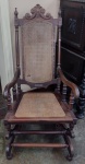 Cadeira de balanço em madeira com molas, encosto com florão entalhado. Assento e encosto com palha indiana (Florão do encosto esta rachado)