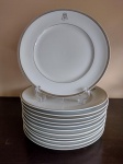 Lote composto de 12 pratos rasos em porcelana branca com friso prateado e monograma JM. Marcado na base "Raquel" - medem 26 cm de diâmetro.
