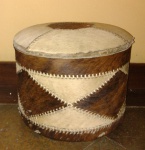 Puff baú no formato circular, revestido com couro de boi nos tons de bege e marrom, pontilhado - mede 36 cm de altura x 47 cm de diâmetro.