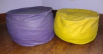Dois puffs estofados em couro sintético sendo um amarelo e outro lilás - mede o maior 30 cm de altura, 45 cm de diâmetro. Obs.: com marcas de uso.
