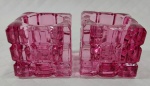Par de castiçais em vidrão de tom rosa decorados por elementos geométricos em alto relevo medindo 5 x 4,5 x 4,5 cm cada.