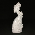 Delicada estatueta de Jovem Dama decorada  com arranjos florais em fina porcelana branca, esmaltada. Exemplar de coleção. Dimensões: 23 cm x 8 cm. 