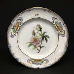 Antigo prato em porcelana esmaltada, possivelmente séc XIX, decorado com flores e figuras de faisão, pintadas à mão. Realces pintados à ouro. Monograma "DB". Presença de restauro na borda. Exemplar de coleção. Dimensões: 24 cm.