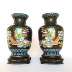 Espetacular e antigo par de vasos Cloisonné  decorado com imagens de Dragão e Fênix sobre fundo preto. Ricos detalhes. Possivelmente séc XIX. Acompanha peanhas em madeira talhada. Exemplares raros e em excelente estado. Dimensões: 26 cm  x 14 cm / sem peanha 22 cm x 14 cm. A técnica do Cloisonné é de origem Bizantina e foi introduzida na China no século XIV / Dinastia Ming. Sobre um objeto fabricado em metal, geralmente em cobre, aplicava-se um conjunto de finos fios dourados formando os contornos dos motivos desejados. Os favos, ou "cloisons", eram depois preenchidos com esmaltes coloridos, fortemente comprimidos e polidos até atingirem o acabamento desejado.