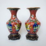 Belo e antigo par de vasos Cloisonné, decorados com arranjos Florais sobre fundo Rouge foncé. Acompanha peanha em madeira talhada. Apresenta pequenas marcas do tempo, nada que tire a beleza do exemplar. Dimensões: 18 cm altura x 9 cm diâmetro.  A técnica cloisonné é de origem bizantina e foi introduzida na China no século XIV / Dinastia Ming.  Sobre um objeto fabricado em metal, geralmente em cobre, aplicava-se um conjunto de finos fios dourados formando os contornos dos motivos desejados. Os favos, ou "cloisons", eram depois preenchidos com esmaltes coloridos, fortemente comprimidos e polidos até atingirem o acabamento desejado.