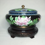 "ARTE ORIENTAL - Antigo centro de mesa  CLOISONNÉ esmaltado e policromado, decorado com peônias ,pássaro, arabescos e estilizados sobre fundo preto . Peanha em madeira talhada.  Acompanha tampa. Exemplar de coleção. Dimensões: 26 cm x 13 cm. A técnica Cloisonné é de origem Bizantina e foi introduzida na China no século XIV / Dinastia Ming. Sobre um objeto fabricado em metal, geralmente em cobre, aplicava-se um conjunto de finos fios dourados formando os contornos dos motivos desejados. Os favos, ou ""cloisons"", eram depois preenchidos com esmaltes coloridos, fortemente comprimidos e polidos até atingirem o acabamento desejado."