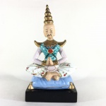 Escultura Oriental em posição de meditação em porcelana esmaltada e rica policromia sobre base em madeira. Dimensões: 24 cm x 13 cm x 12 cm.