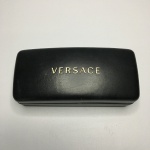 VERSACE - Estojo emborrachado para óculos de sol Versace com inscrição em dourado e parte interna aveludada com inscrição em preto brilhante. Acompanha lenço com marca impressa. Dimensões: 6 cm x 7 cm x 16 cm.