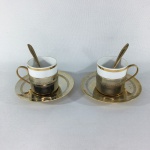 Antigo par de xícaras para café em porcelana filetada à Ouro. Suporte e pires em metal dourado decorados com faixa Grega incrustadas. Acompanha duas colheres. Presenças de manchas do tempo. Dimensões:  Xícaras 6 cm / Capacidade para 60 ml e Pires 10 cm.