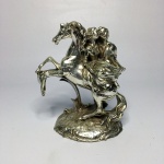 Escultura em resina metalizada na cor prata de cavalo e casal em cena romântica. Sinais de desgastes. Dimensões: 13 cm.