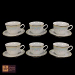 SEIS  XÁVENAS PARA CHÁ EM PORCELANA BRANCA COM RESPECTIVOS PIRES,DECORAÇÃO FLORAL SOBRE FUNDO AZUL-CLARO E FAIXAS EM AMARELO E DOURADO DA MANUFATURA GERMER. UMA APRESENTA  BICADONA BORDA E OUTRS FIODE CABELO.