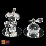 DUAS ESCULTURAS EM CRISTAL REPRESENTANDO CHAMPANHEIRA  COM DUAS TAÇAS E PERFUMEITO, EM BASE CIRCULAR ESPELHADA- MED TOTAL: 5,5 X 5 CM E 4 X 5 CM.