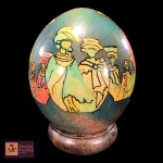 BELÍSSIMO OVO DECORATIVO EM PORCELANA VITRIFICADA, COM DECORAÇÃO DE MULHERES AFRICANAS EM POLICROMIA, ASSINADO POR ANA E DATADO DE 2006, SOBRE BASE DE MADEIRA CIRCULAR. - MED 17 X 12 CM.