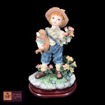 GRUPO ESCULTÓRICO  EM RESINA REPRESENTANDO GAROTO COM CACHORROS E FLORES EM BASE OVAL - MED: 17,5 X 11 X 8 CM.