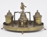 Antigo tinteiro em metal dourado com  recipientes para tintas, sendo o segundo encimado com escultura retratando figura, base oval apoiada por 04 pés recurvos. med: 26 x 17 x 19cm