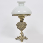 Abajour de mesa dito Lampião com estrutura em bronze dourado, cinzelado e filigranado, decorado com motivos fitomórficos e base com 3 pés recurvos com galeria com camafeu de leão e com cúpula em vidro opalinado no tom branco. Med: 60cm